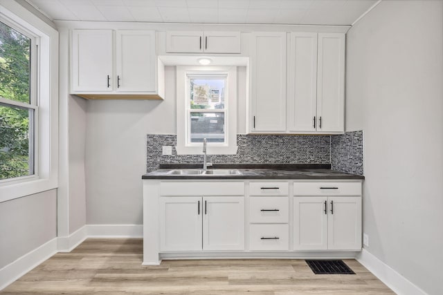 kitchen with tasteful backsplash, dark countertops, visible vents, a sink, and baseboards