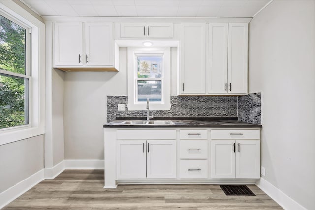 kitchen with baseboards, visible vents, dark countertops, a sink, and backsplash