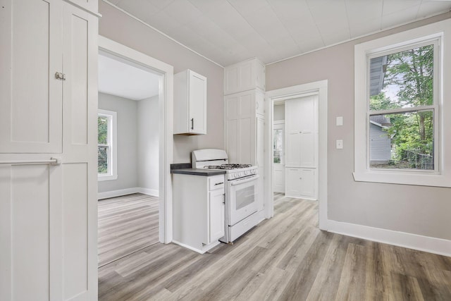 kitchen with light wood finished floors, baseboards, white range with gas stovetop, and white cabinetry