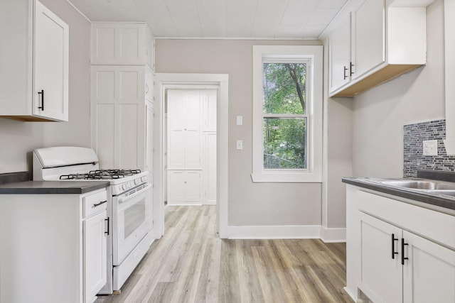 kitchen with white range with gas cooktop, tasteful backsplash, white cabinets, dark countertops, and light wood-style floors