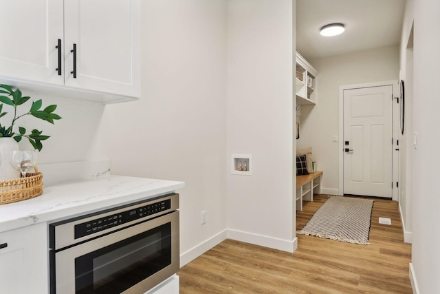 kitchen featuring light wood-type flooring, oven, white cabinetry, and light stone counters