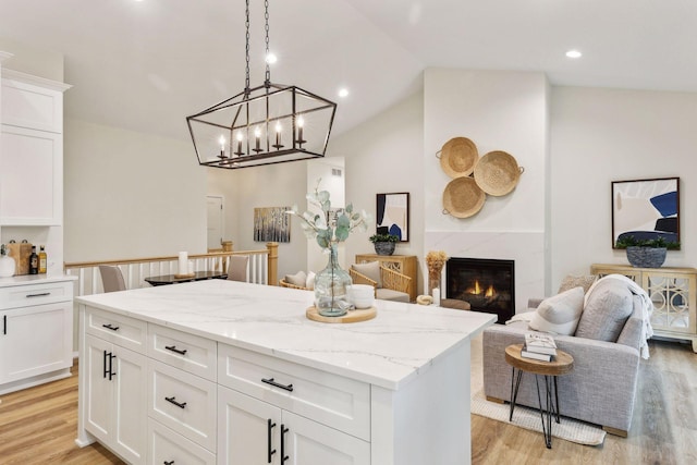 kitchen featuring lofted ceiling, a high end fireplace, decorative light fixtures, light hardwood / wood-style floors, and white cabinetry