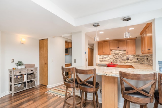 kitchen featuring kitchen peninsula, backsplash, a breakfast bar, decorative light fixtures, and dark hardwood / wood-style floors