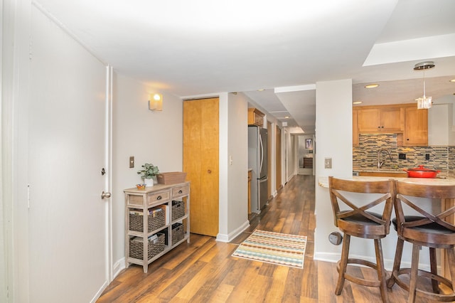 interior space with dark wood-type flooring, sink, hanging light fixtures, decorative backsplash, and stainless steel refrigerator