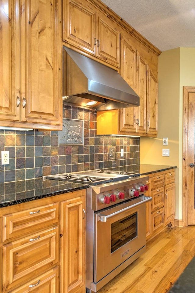 kitchen with designer range, backsplash, light hardwood / wood-style floors, and dark stone counters