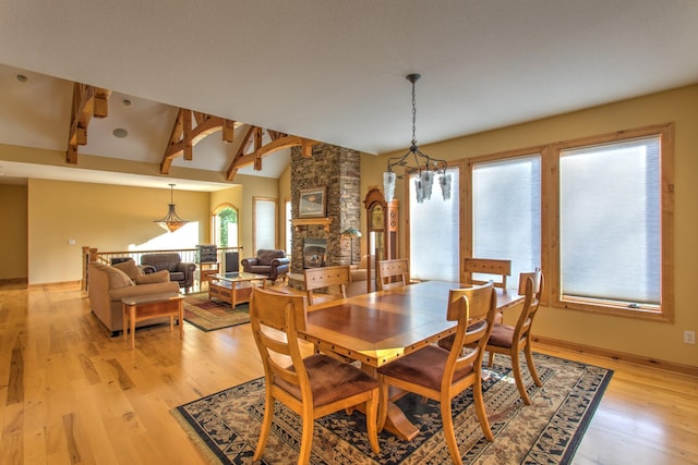 dining area featuring vaulted ceiling with beams, an inviting chandelier, a stone fireplace, and light hardwood / wood-style flooring