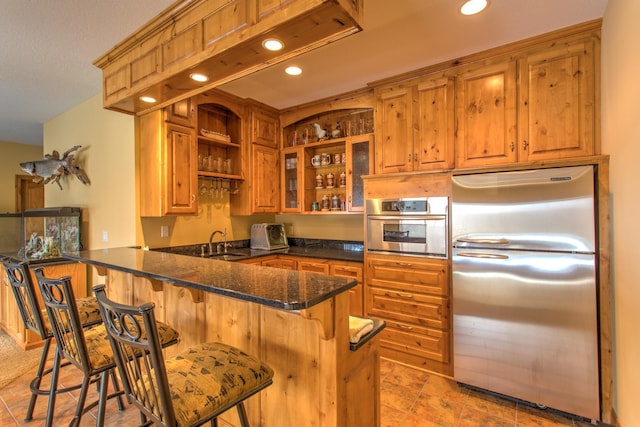 kitchen with dark stone counters, sink, a kitchen bar, kitchen peninsula, and stainless steel appliances