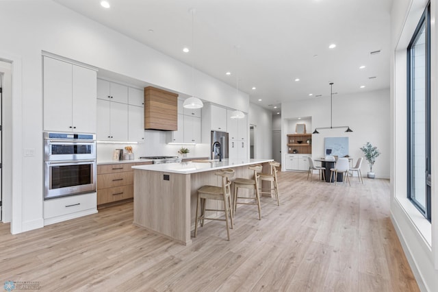 kitchen with light wood-type flooring, stainless steel double oven, white cabinetry, hanging light fixtures, and a large island