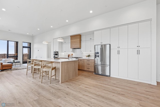 kitchen with white cabinets, a spacious island, hanging light fixtures, light wood-type flooring, and high end fridge