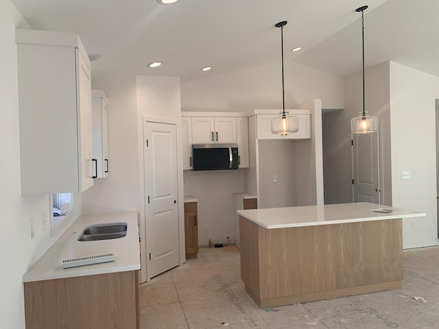 kitchen featuring vaulted ceiling, decorative light fixtures, white cabinetry, sink, and a center island