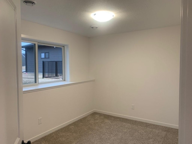 empty room with carpet flooring, a textured ceiling, baseboards, and visible vents