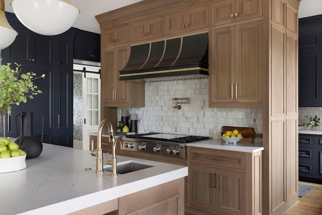 kitchen with decorative backsplash, custom exhaust hood, stainless steel gas cooktop, a barn door, and light hardwood / wood-style floors