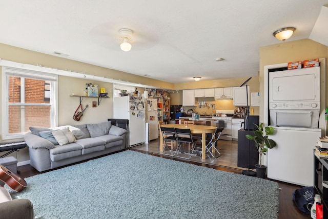 living room with stacked washer and dryer, vaulted ceiling, and dark hardwood / wood-style floors