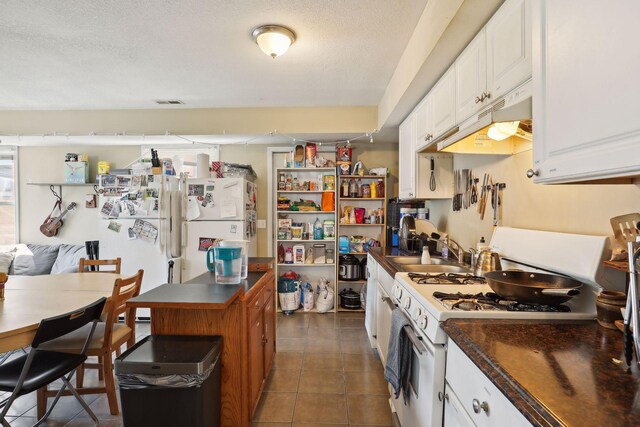 kitchen featuring white appliances, dark tile patterned flooring, sink, a textured ceiling, and white cabinetry