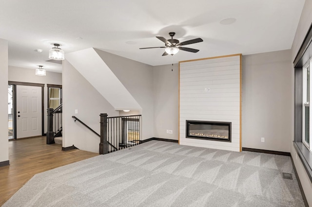 living room featuring a large fireplace, visible vents, baseboards, wood finished floors, and carpet flooring