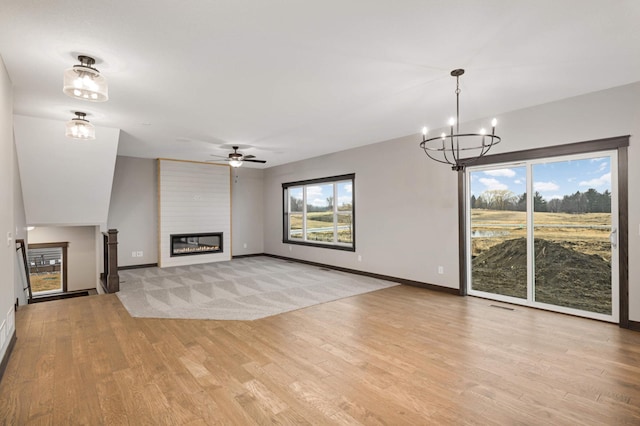 unfurnished living room with ceiling fan with notable chandelier, a fireplace, visible vents, baseboards, and light wood-type flooring