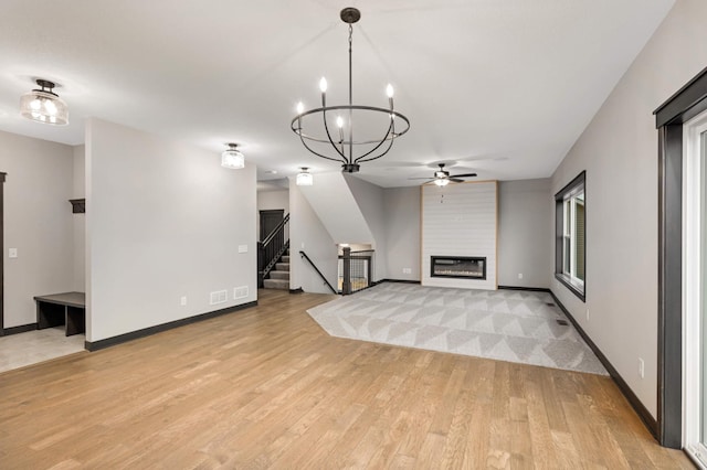 unfurnished living room featuring light wood finished floors, baseboards, a fireplace, and stairway