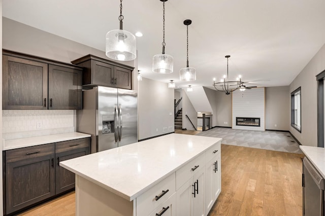 kitchen featuring a fireplace, light countertops, hanging light fixtures, dark brown cabinetry, and stainless steel fridge