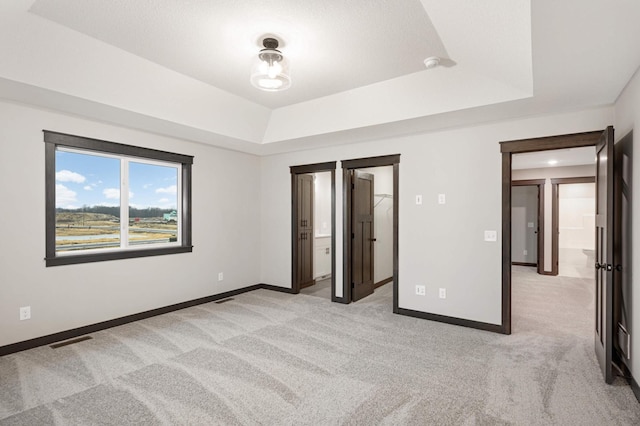 unfurnished bedroom with baseboards, a raised ceiling, visible vents, and light colored carpet