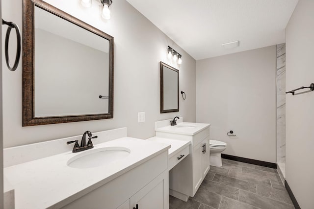 full bath with baseboards, two vanities, a sink, and toilet