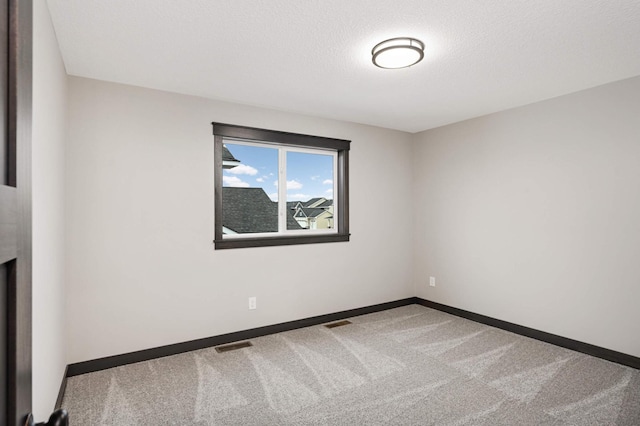 carpeted spare room with visible vents, baseboards, and a textured ceiling