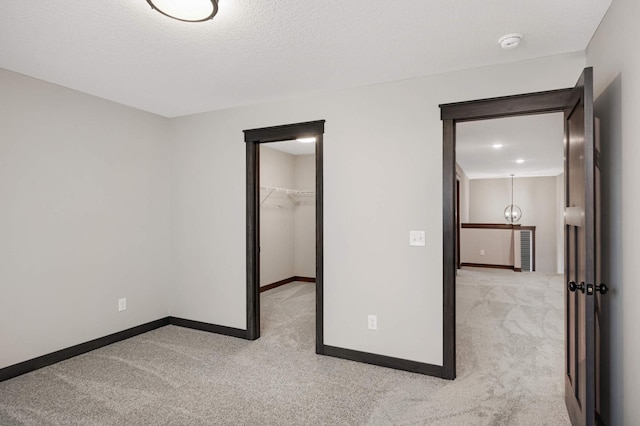 unfurnished bedroom featuring carpet floors, a walk in closet, a closet, a textured ceiling, and baseboards