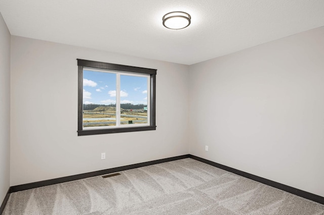 unfurnished room with carpet floors, visible vents, a textured ceiling, and baseboards