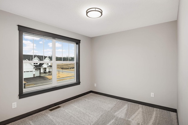 spare room featuring carpet, a textured ceiling, visible vents, and baseboards