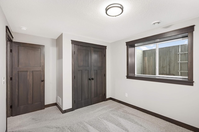 unfurnished bedroom featuring carpet, a closet, a textured ceiling, and baseboards