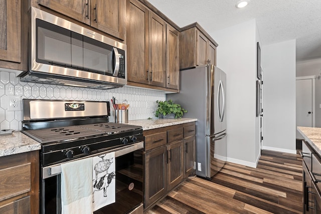 kitchen featuring decorative backsplash, appliances with stainless steel finishes, light stone counters, and dark wood-type flooring