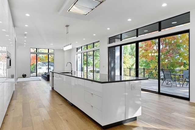 kitchen with decorative light fixtures, sink, white cabinets, a large island, and light wood-type flooring