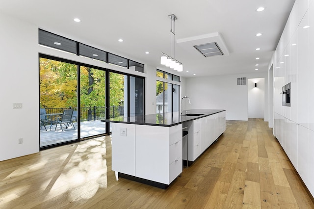 kitchen with sink, hanging light fixtures, a kitchen island with sink, light hardwood / wood-style floors, and white cabinets