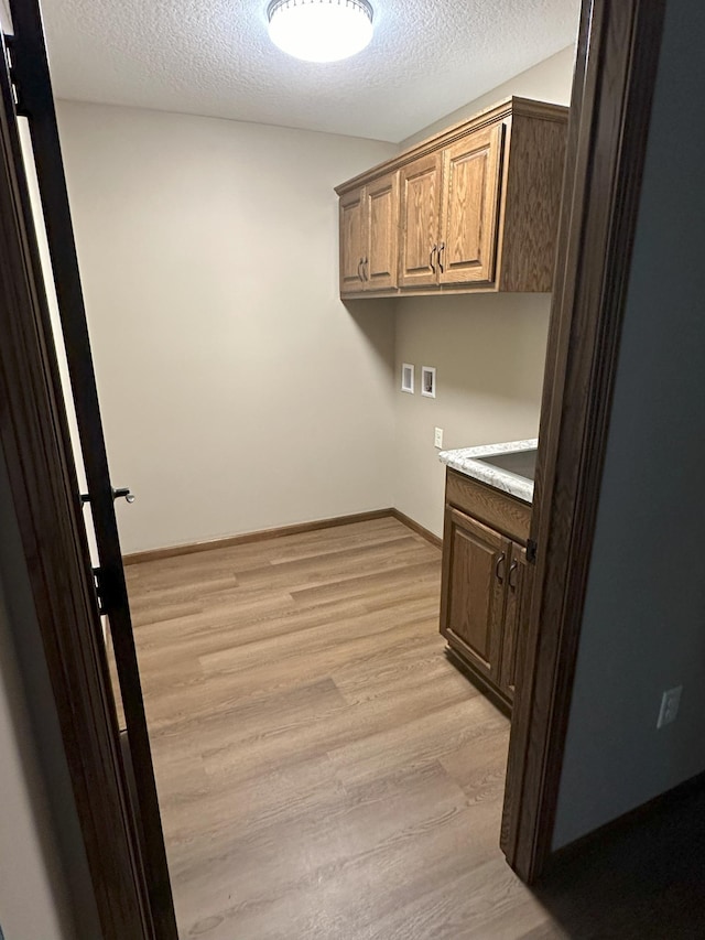 clothes washing area featuring sink, cabinets, light hardwood / wood-style flooring, hookup for a washing machine, and a textured ceiling