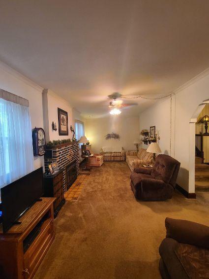 living room with carpet, a brick fireplace, ceiling fan, and crown molding