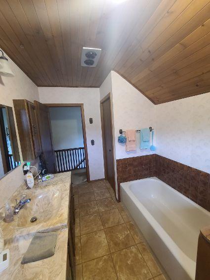 bathroom featuring wooden ceiling, tile patterned flooring, a bath, lofted ceiling, and vanity