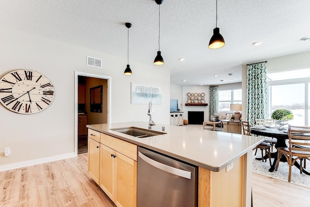 kitchen featuring light brown cabinetry, light wood-type flooring, stainless steel dishwasher, sink, and an island with sink