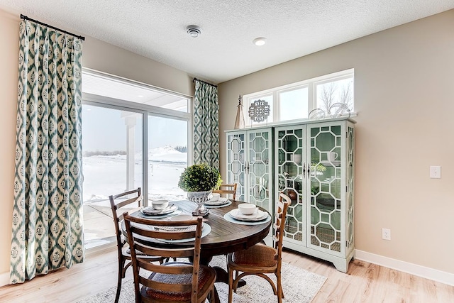 dining area with light wood-type flooring, a textured ceiling, and baseboards