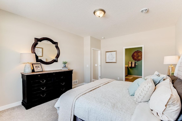 bedroom featuring baseboards, visible vents, light colored carpet, ensuite bathroom, and a textured ceiling