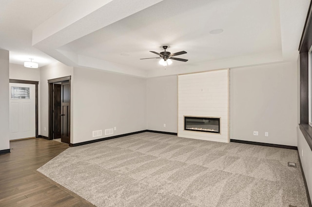 unfurnished living room with a large fireplace, baseboards, a raised ceiling, and a ceiling fan