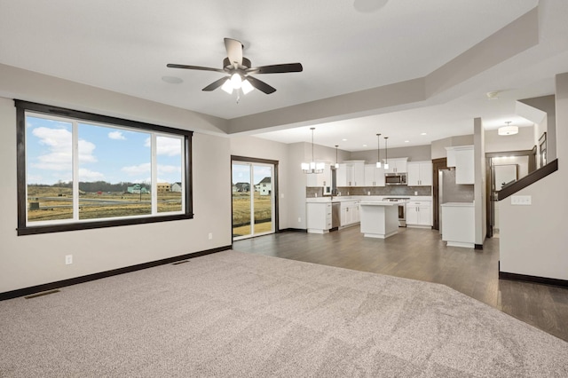 unfurnished living room with ceiling fan with notable chandelier, dark wood-type flooring, visible vents, and baseboards