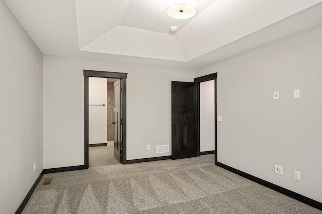 unfurnished bedroom featuring a tray ceiling, carpet, visible vents, and baseboards