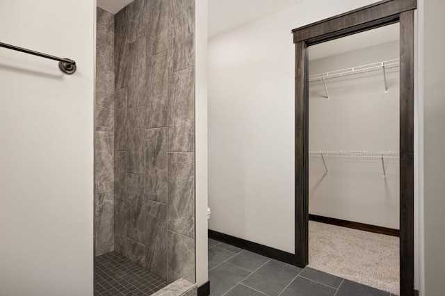 full bath featuring tiled shower, tile patterned floors, a walk in closet, and baseboards