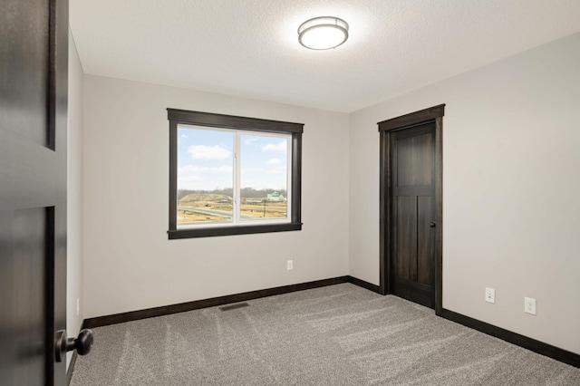 carpeted empty room featuring baseboards, visible vents, and a textured ceiling