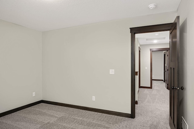 empty room with visible vents, baseboards, a textured ceiling, and light colored carpet