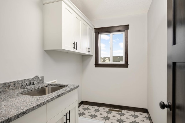 laundry area with light floors, cabinet space, a sink, a textured ceiling, and baseboards