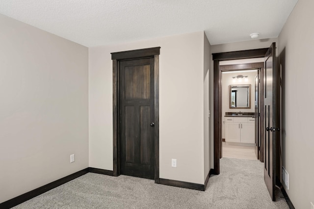 unfurnished bedroom with a textured ceiling, light carpet, a sink, visible vents, and baseboards