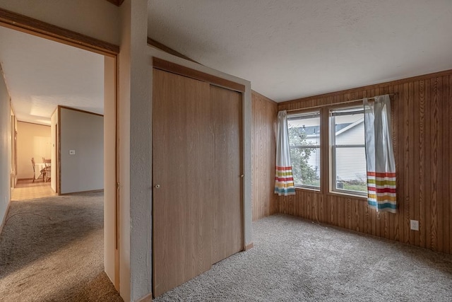 unfurnished bedroom with wood walls, a closet, and light carpet