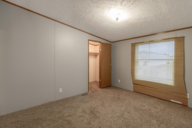 unfurnished bedroom with carpet, a walk in closet, a textured ceiling, vaulted ceiling, and a closet