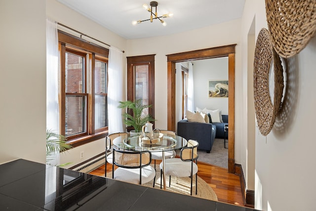 dining space with hardwood / wood-style flooring, a baseboard heating unit, and a notable chandelier