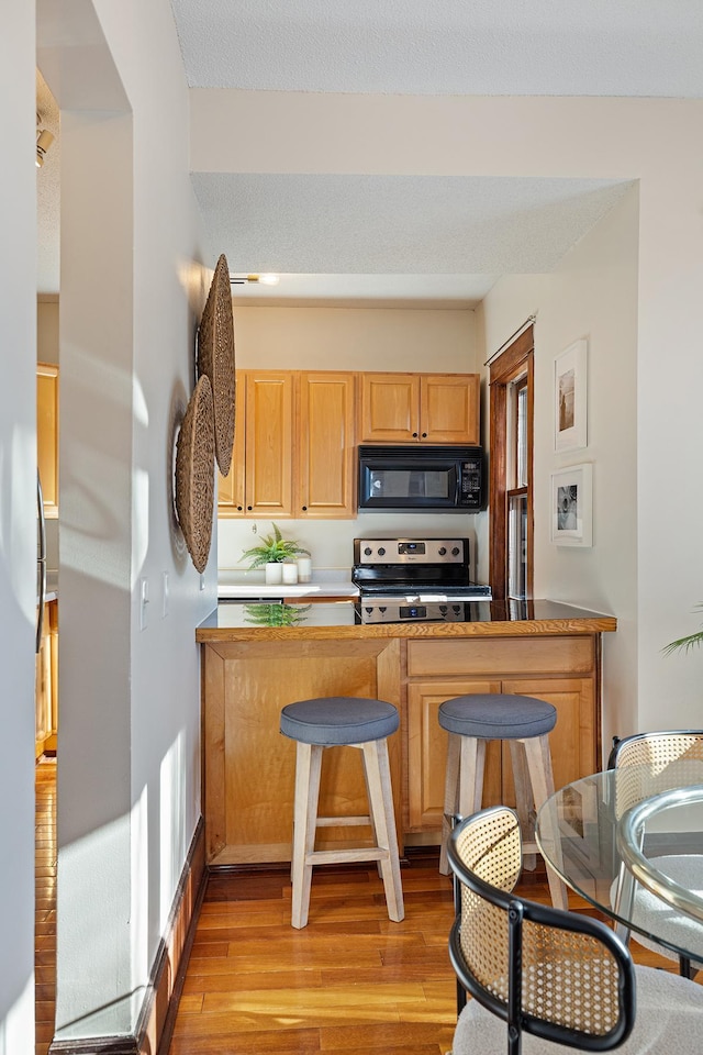 kitchen with stainless steel range with electric stovetop, light brown cabinetry, light hardwood / wood-style floors, and kitchen peninsula